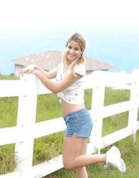 Blonde teenager unclothes infront of a fence for cows