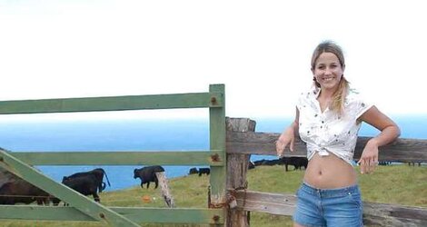Blonde teenager unclothes infront of a fence for cows